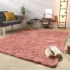 A living room scene with a pink rug, a gray armchair, side tables, and a shelf. Produktbild-Vorschau