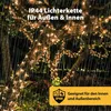 A string of warm white fairy lights wrapped around tree branches at night, with rain falling. Produktbild-Vorschau
