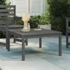 A dark gray wooden coffee table sits on a patio next to a matching chair, with plants and a building in the background. Podgląd zdjęcia produktu