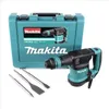 A Makita rotary hammer and its accessories are displayed on a white background, with the product's carrying case in the background. Podgląd zdjęcia produktu