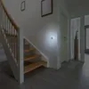A night light is plugged into a wall socket next to a staircase in a hallway. Voir les images du produit
