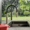 A modern kitchen sink with a flexible faucet, overlooking a lush green garden through a large window. Náhled obrázku produktu