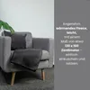 A gray armchair with a dark gray fleece blanket and a dark gray pillow on it, next to a large green leaf plant. Náhľad obrázku produktu