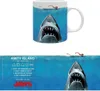 A mug with a Jaws movie theme, showing a shark and a swimmer, with care instructions and movie title on a separate strip below. Anteprima dell’immagine prodotto