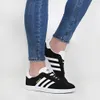 A person wearing blue jeans and black Adidas Gazelle sneakers. Produktbild-Vorschau