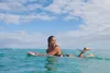 A woman is lying on a surfboard in the ocean. Produktbild-Vorschau