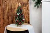 A small, decorated Christmas tree sits on a table in front of a wooden wall. Voir les images du produit