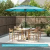 A patio set with a large turquoise umbrella, round wooden table, and four wooden chairs, set on a patio with a wooden fence and greenery in the background. Podgląd zdjęcia produktu