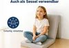 A young girl is sitting on a folded mat, which is set up as a chair, in front of a white wall. Produktbild-Vorschau