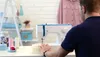 A person is using a sewing machine in a well-lit room with shelves in the background. Produktbild-Vorschau