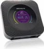 A black Netgear Nighthawk M1 mobile hotspot router is shown from a slightly elevated front-left angle, resting on a reflective surface. The device has a circular screen displaying usage statistics and connectivity information. Náhľad obrázku produktu