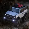 A white remote-controlled Ford Bronco toy car is driving on a rocky, natural terrain. Podgląd zdjęcia produktu