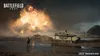 A soldier stands in a muddy field, facing a massive explosion in the distance. Two tanks are visible in the midground, one in focus and the other further back. The sky is dark and stormy. Produktbild-Vorschau