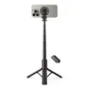 A black selfie stick with a tripod base and a smartphone attached is shown against a white background. A small black remote control is also visible. Produktbild-Vorschau
