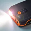 A close-up shot of a black and orange jump starter power bank with its flashlight on. Náhled obrázku produktu