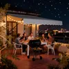 A group of friends enjoying a barbecue on a balcony at night, with a city skyline in the background. Produktbild-Vorschau