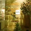 A decorative display featuring string lights, vases with artificial flowers, and a small Christmas tree against a wooden wall. Produktbild-Vorschau