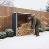 A man is stacking firewood in a log store next to a wooden fence in a snowy garden. Podgląd zdjęcia produktu