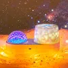 A projector lamp with two domes, one projecting blue and purple light, the other projecting white and yellow light, set against a starry night sky background. Produktbild-Vorschau