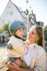 A woman is holding a child wearing a helmet. Voir les images du produit