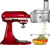 A red KitchenAid Artisan stand mixer with a silver food processor attachment is shown, with chopped vegetables falling into a glass bowl. Podgląd zdjęcia produktu
