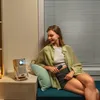 A young woman sits on a bench next to a projector, holding a remote control. Produktbild-Vorschau