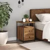 A bedside table with drawers next to a bed, with a plant and lighting in the background. Voir les images du produit