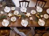 A beautifully set dining table for a festive meal, likely for Christmas, with plates, cutlery, napkins, and decorative elements like pine sprigs and reindeer figurines. Produktbild-Vorschau