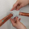 Hands are shown installing a white pipe insulation piece onto two copper pipes. Produktbild-Vorschau