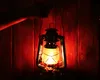 A hand holding a lit petroleum lantern in front of a wooden wall. Náhľad obrázku produktu