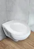 A white wall-mounted toilet with a closed lid, set against a concrete wall and wooden floor. Produktbild-Vorschau