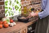 A person is cooking in a kitchen with a glass splashback showing plants. Náhľad obrázku produktu
