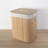 A laundry basket made of bamboo with a fabric liner and lid, placed on a wooden floor against a white wall. Podgląd zdjęcia produktu