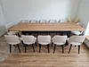 A dining set with a large wooden table and multiple chairs arranged around it in a room with light-colored walls and wooden flooring. Produktbild-Vorschau