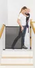 A woman is holding a child while standing on stairs next to a baby gate. Náhľad obrázku produktu