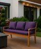 A purple cushion set on a wooden outdoor sofa on a deck, with greenery and a house in the background. Náhľad obrázku produktu