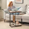 A woman is using a laptop while sitting on a couch, with a side table next to her that has a cat bed underneath. Produktbild-Vorschau