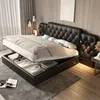 A modern bedroom with a black upholstered bed frame, featuring a hydraulic lift mechanism revealing storage space underneath. The bed is made with white and gray bedding.