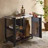 An outdoor serving cart with various kitchen items and ingredients, set up on a stone patio. Produktbild-Vorschau