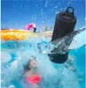 A portable Bluetooth speaker is shown partially submerged in a swimming pool with children playing in the water. Náhled obrázku produktu