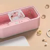A pink ultrasonic cleaner with jewelry inside, surrounded by other jewelry pieces on a beige surface. Náhled obrázku produktu
