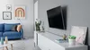 A modern living room with a blue sofa, a white media console, and a TV mounted on the wall. Podgląd zdjęcia produktu