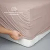 A hand is shown stretching a fitted sheet over a mattress, demonstrating its fit. Produktbild-Vorschau