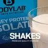 A close-up shot of a glass of protein shake next to a bag of BODYLAB Whey Protein Isolat. Produktbild-Vorschau