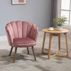 A pink velvet accent chair sits next to a small wooden side table with a plant and a cup of coffee on it, in a room with a grey wall and a window. Náhľad obrázku produktu