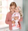 A young girl is holding a baby doll in a room with soft lighting. Produktbild-Vorschau