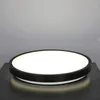 A round LED ceiling light with a black rim sits on a dark surface against a gray background. Voir les images du produit