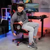 A man is sitting in a gaming chair in a room with gaming equipment. Náhled obrázku produktu