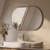 A modern bathroom vanity with a rectangular sink, a gold faucet, and an oval mirror with a gold frame. Dried floral arrangement in a vase is on the left, and folded towels are on the right. Náhled obrázku produktu
