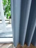 A close-up view of a blue curtain hanging by a window, with a plant visible in the background. Produktbild-Vorschau